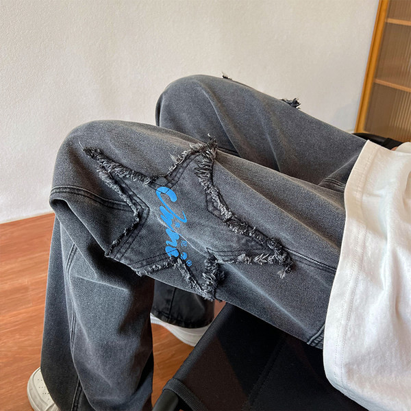 Széles szabású férfi farmernadrág szakadt motívumokkal és feliratokkal